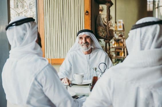 Traja obchodníci si vychutnávajú čaj v Dubaji v tradičných emirátskych odevoch.