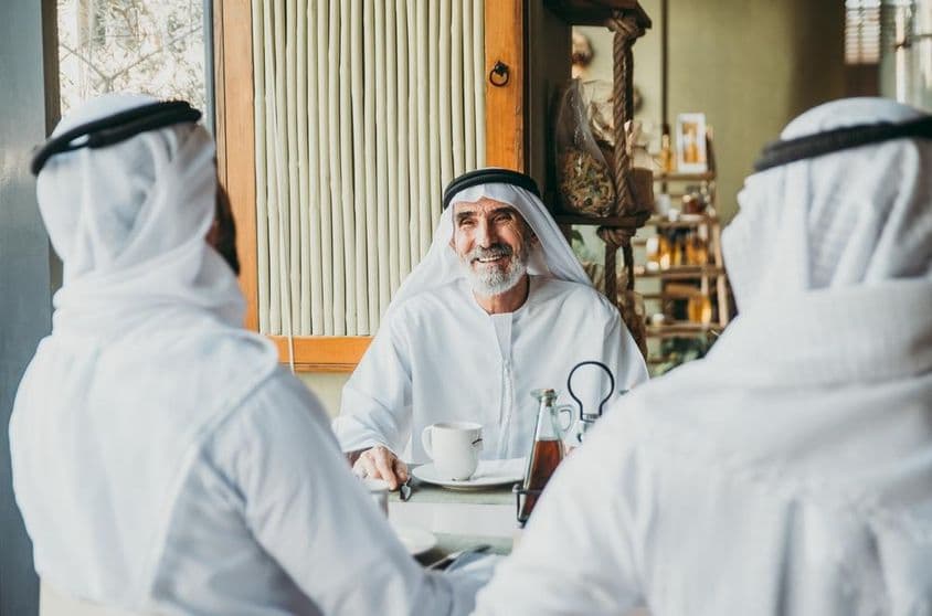 Traja obchodníci si vychutnávajú čaj v Dubaji v tradičných emirátskych odevoch.