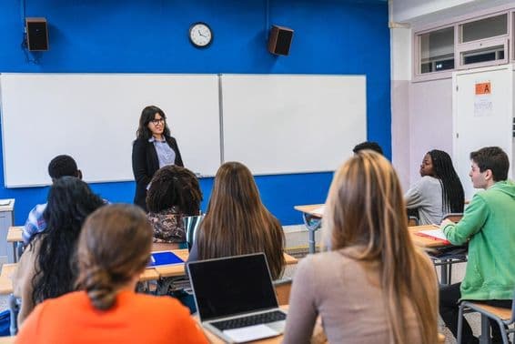 Stredoškolskí študenti počúvajú učiteľa, ktorý prednáša lekciu v modernej triede.