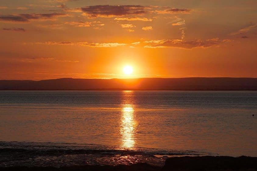 Západ slnka odrážajúci sa na vode a oblakoch počas letného slnovratu.