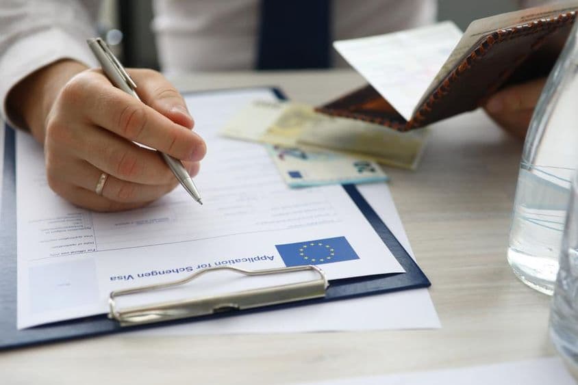 Muž držiaci pas a vkladá osobné údaje do žiadosti o schengenské víza.