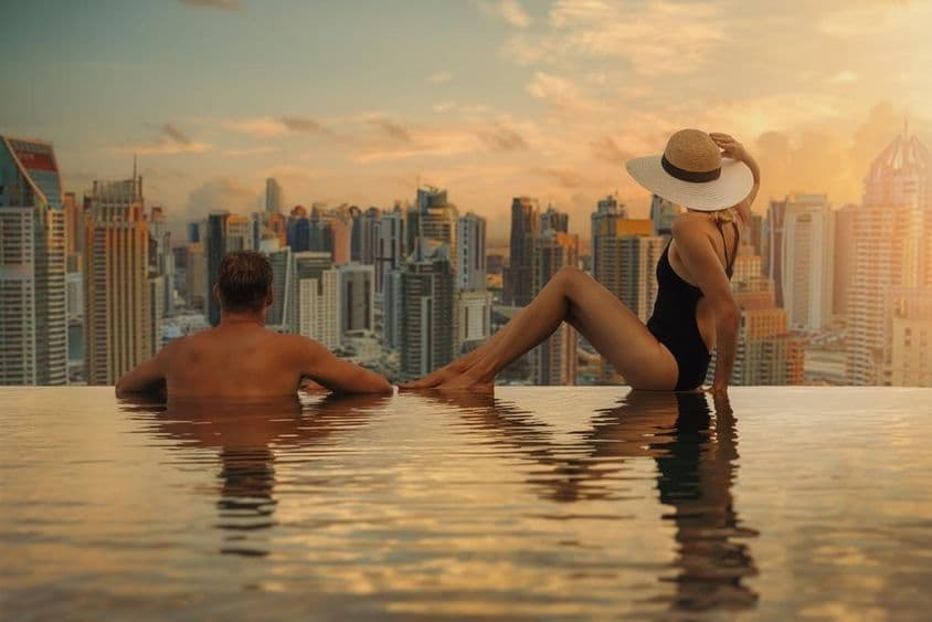 Pár si užíva panorámu Dubaja so stohpatrovou architektúrou z nekonečného bazéna pri západe slnka.