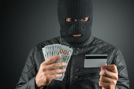 Zločinec v lyžiarskej maske držiaci kreditnú kartu proti tmavému pozadiu.