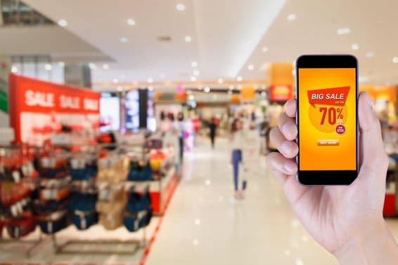 Smartfón so zobrazením aplikácie veľkého výpredaja na rozmazanom pozadí obchodného centra.