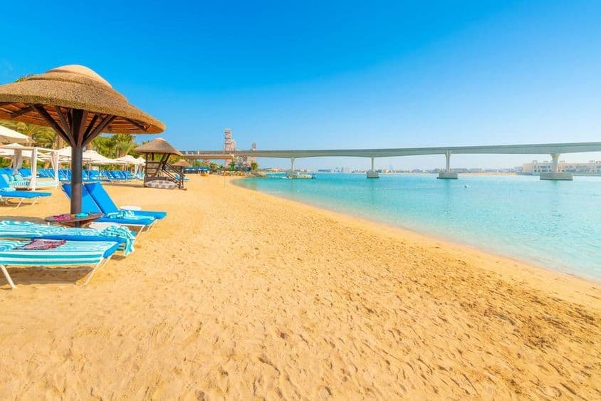 Na piesočnatej pláži Arabského zálivu, monorail Palm Jumeirah Island prechádza ponad more v Dubaji.