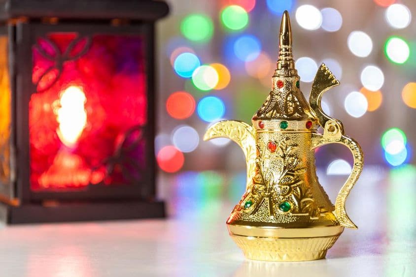 Arabská kávová kanvica a lampa s farebnými, rozmazanými svetlami v pozadí.