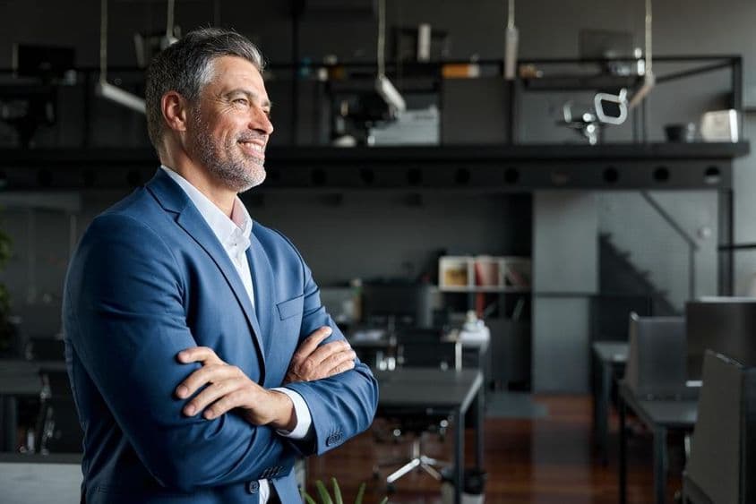 Biznisman CEO v obleku stojí v kancelárii s prekríženými rukami.