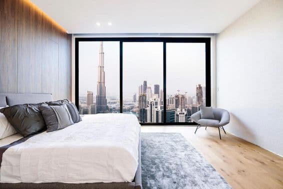 Moderná spálňa s bielym stropom a drevenou dekoráciou, pohľad na výškovú budovu a centrum Dubaja.