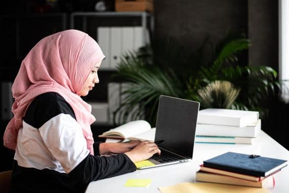 Krásna muslimská žena študuje doma pomocou laptopu.