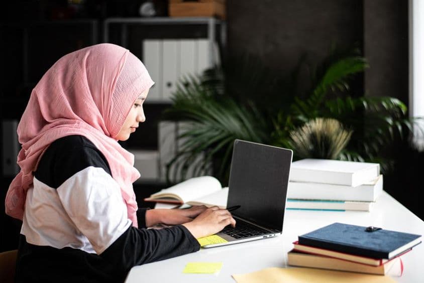 Krásna muslimská žena študuje doma pomocou laptopu.