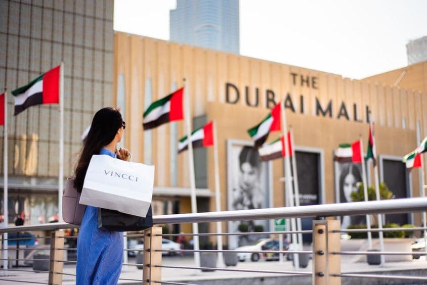 Ázijský turista s nákupnými taškami pri hlavnom vstupe do Dubai Mall.