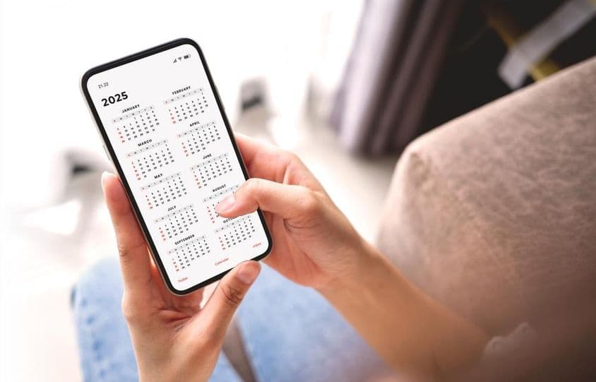 Podnikateľka plánujúca aktivity na rok 2025 s mobilom a mesačným kalendárom.