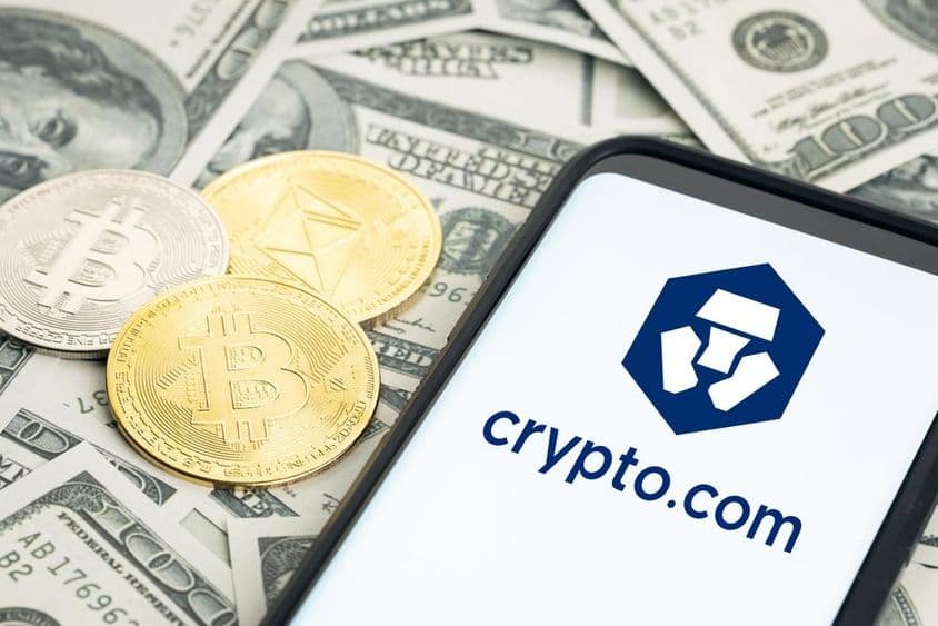 Logo Crypto.com, dolárové bankovky, mince Bitcoin a Ethereum viditeľné.