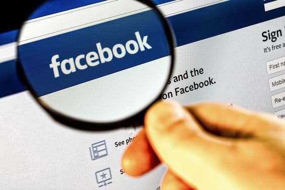 Úvodná stránka Facebooku na monitore cez zväčšovacie sklo.