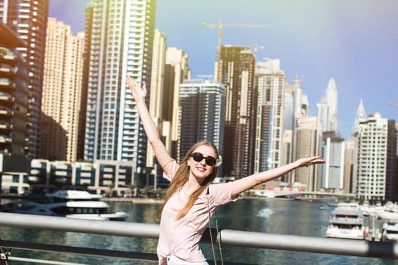 Slnko osvetľuje štýlovú ženu, ktorá zdvíha ruku na moste niekde v Dubaji.