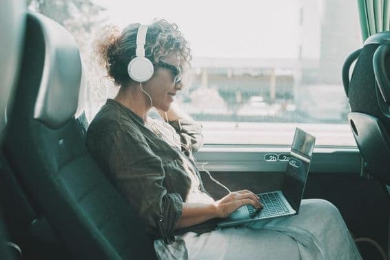 Mladá žena pracujúca na prenosnom počítači so slúchadlami na sedadle autobusu.
