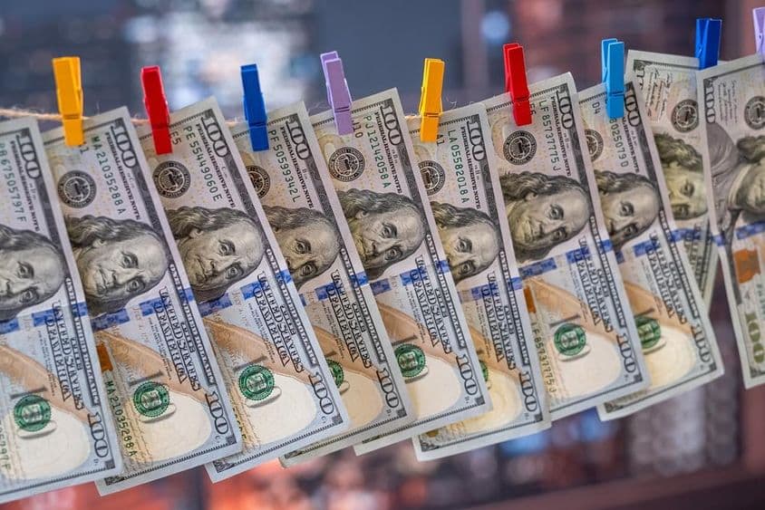 Bankovka 100 amerických dolárov zavesená na šnúre s drevenými štipcami.