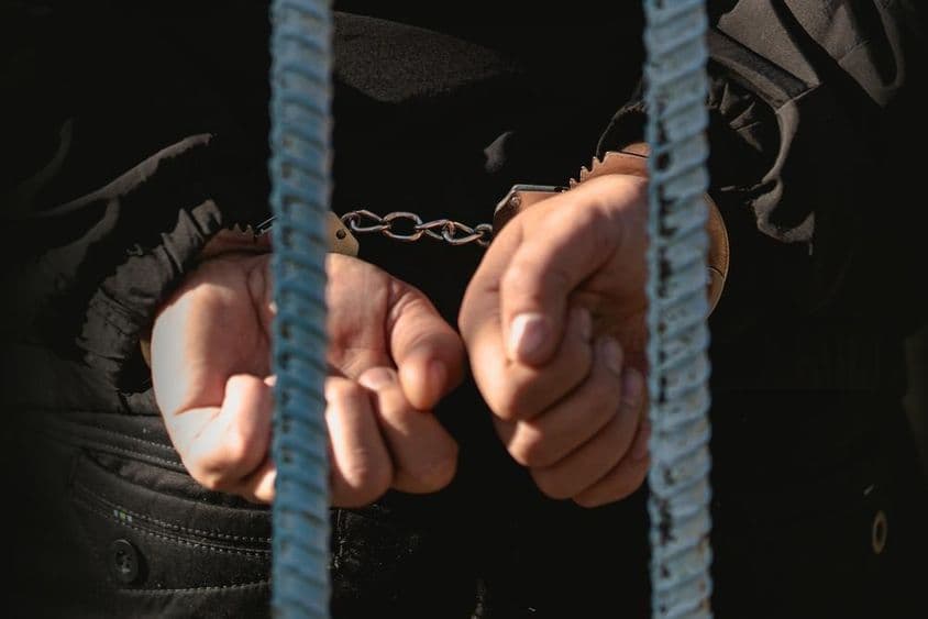 Muž so spútanými rukami za mrežami na policajnej stanici.