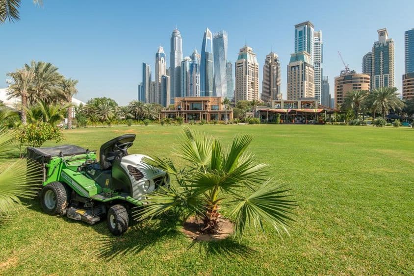 Kosačka na traktore na zelenej lúke pred mrakodrapmi v Dubai Marina.