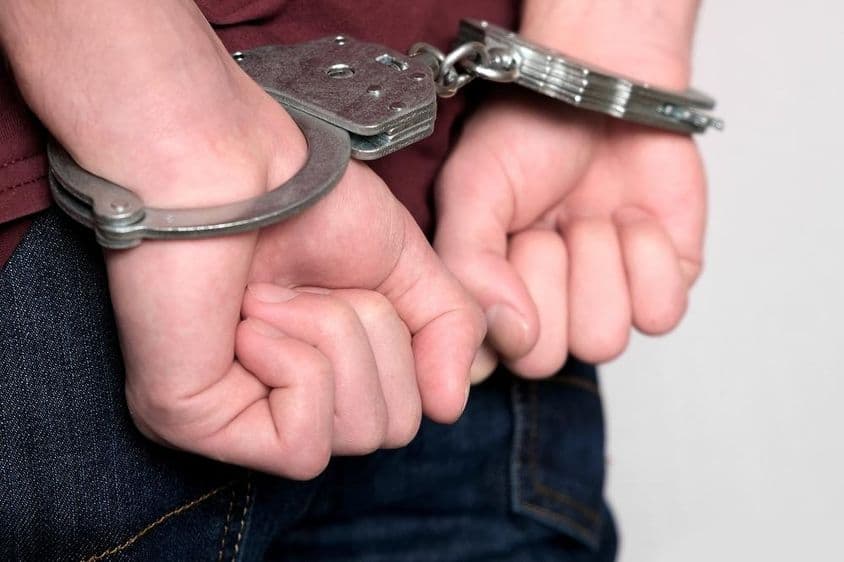Zločinec so spútanými rukami a zatknutý.