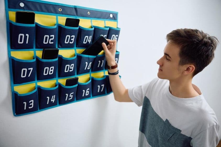 Žiak odovzdáva smartfón do nástenného organizéra na telefóny.