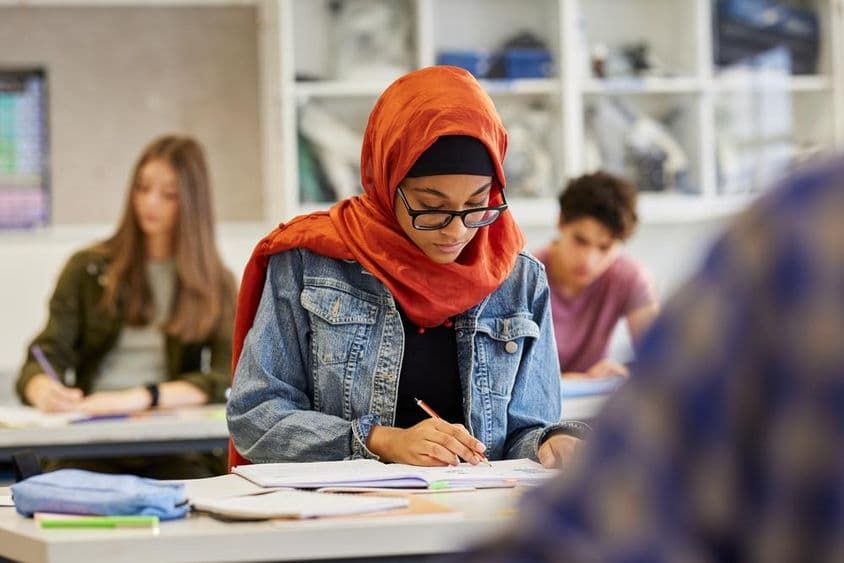 Mladá študentka v hijabe si zapisuje poznámky.