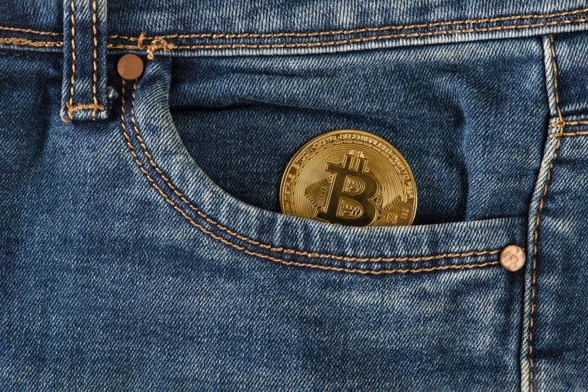 Zlatá bitcoinová minca leží v vrecku riflí.
