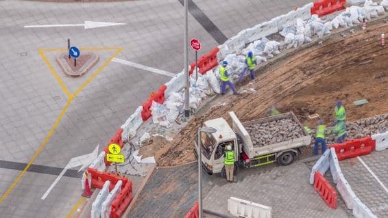 Proces opravy chodníka s viacerými robotníkmi a zariadeniami, ktoré rozoberajú chodník a betón.