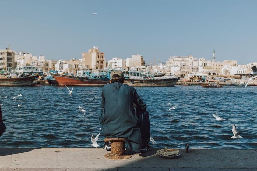 Muž si užíva výhľad na nábrežie s loďami a čajkami v Dubai Creek.