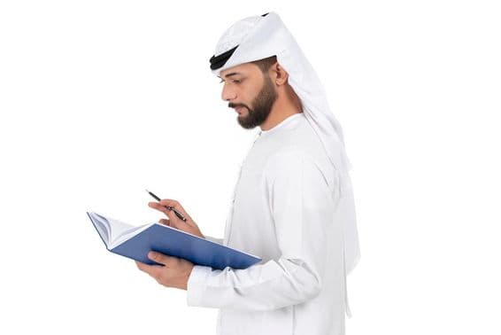 Mladý arabský učiteľ stojaci a píšuci do knihy.