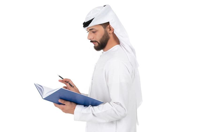 Mladý arabský učiteľ stojaci a píšuci do knihy.