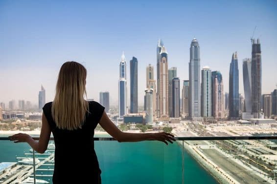 Žena v čiernom s premýšľavým výrazom na balkóne s výhľadom na mrakodrapy v Dubaji, Spojené arabské emiráty.