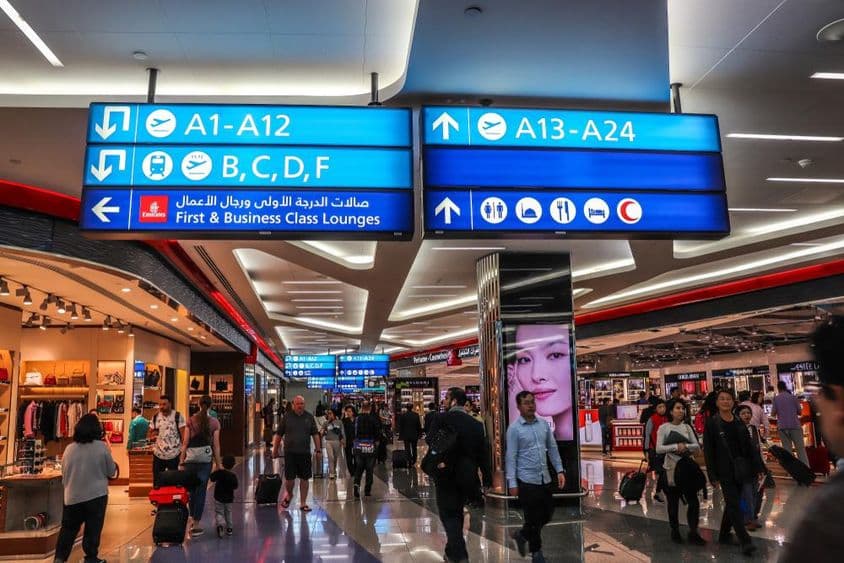 Cestujúci kráčajúci smerom k odletovým bránam na Medzinárodnom letisku Dubaj (DXB).