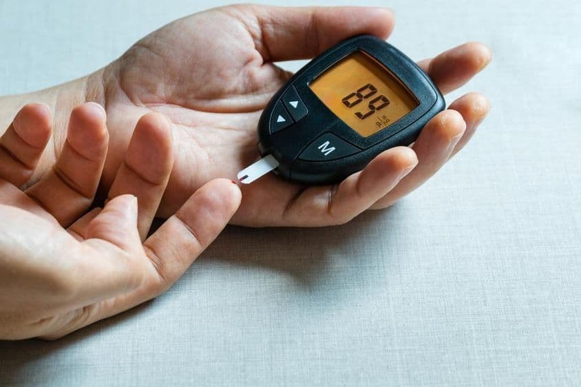 Ruky muža používajúceho digitálny glukomer na monitorovanie cukrovky.