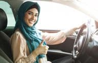 Šťastná arabská žena v hidžábe riadiaca auto so zdvihnutým palcom.