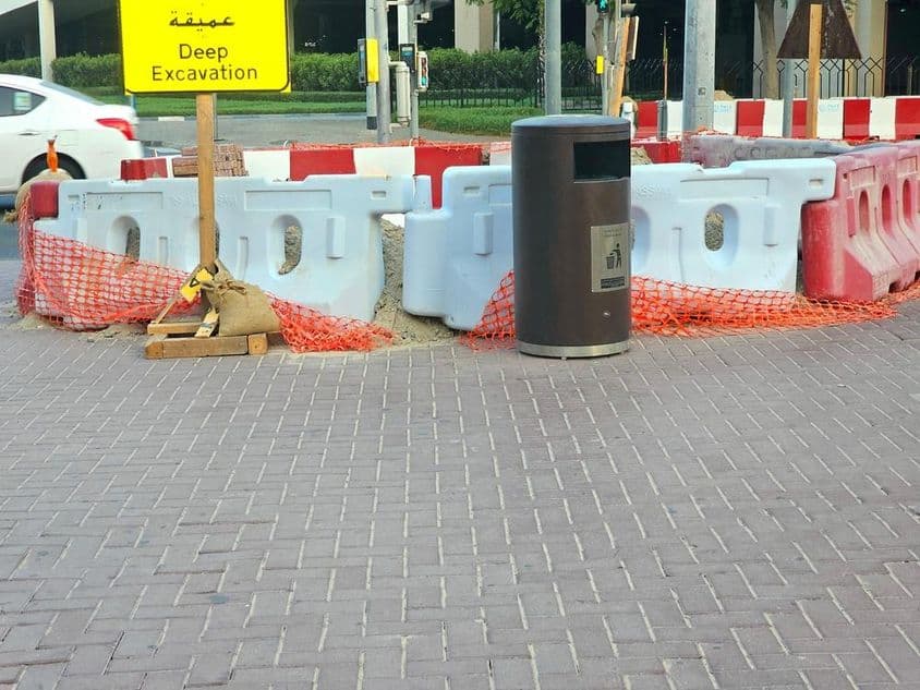 Oprava cesty obklopená plastovými bariérami a oranžovou bezpečnostnou sieťou.