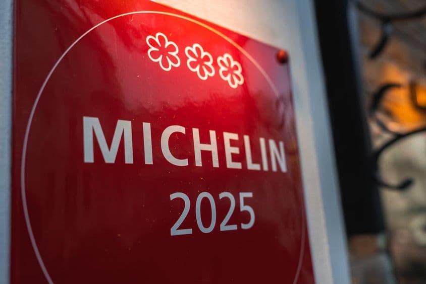 Červená, trojhviezdičková Michelin plaketa 2025 na svetlej stene.