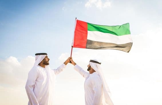 Arabskí muži v kandúrách kráčajúci v púšti s vlajkou.