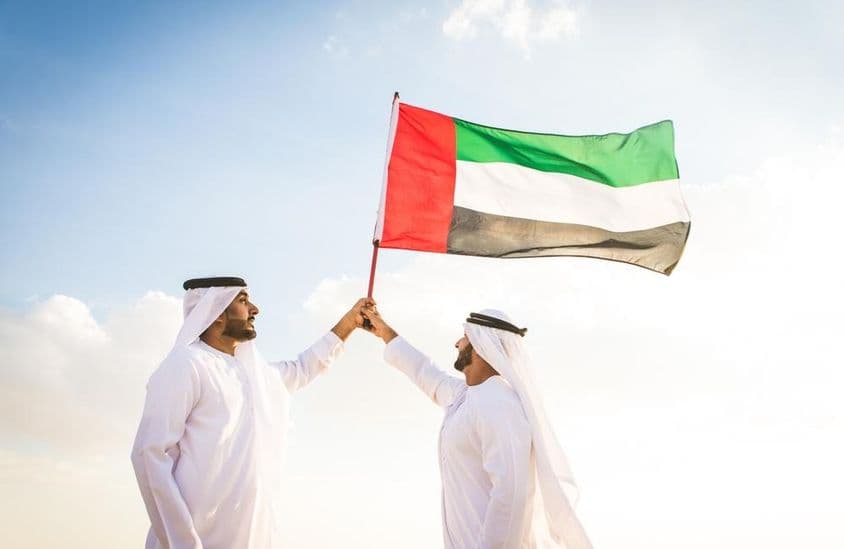 Arabskí muži v kandúrách kráčajúci v púšti s vlajkou.