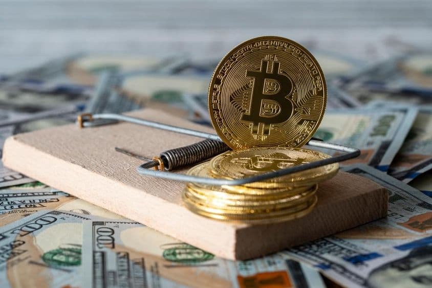 Zlaté mince kryptomeny bitcoin v pasci na myši s americkými bankovkami v pozadí.