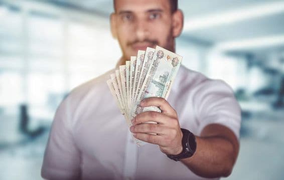 Muž držiaci dirhamové bankovky, stojaci pred bankovou pobočkou.