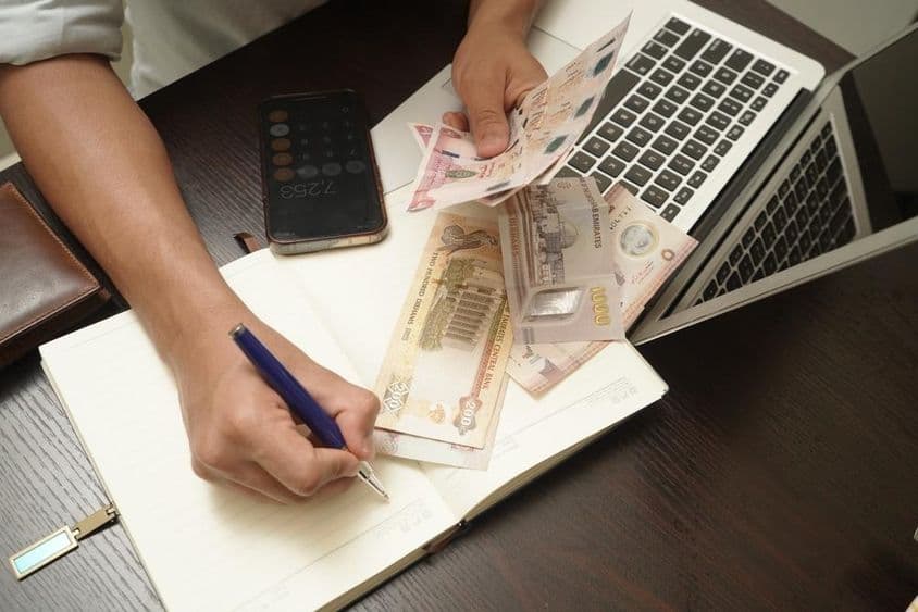 Muž sedí pri stole a počíta balík bankoviek SAE dirham.
