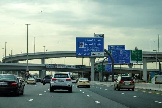 Dubajská cesta s autami a reklamným nadjazdom.