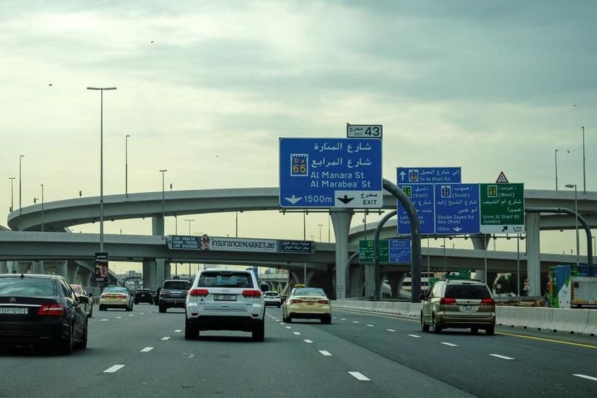 Dubajská cesta s autami a reklamným nadjazdom.
