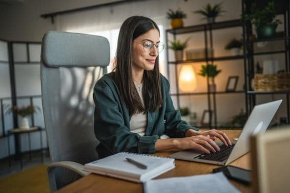 Dospelá žena pracujúca na notebooku a používajúca zápisník v domácej kancelárii.