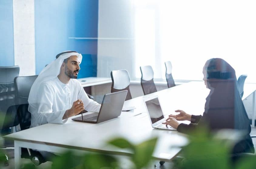 Muž a žena v tradičnom oblečení pracujúci v dubajskej obchodnej kancelárii.