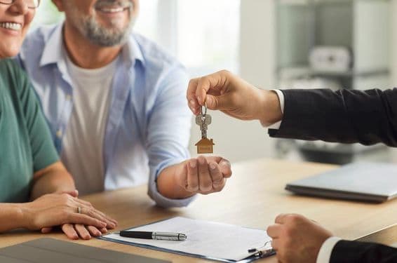 Realitný agent odovzdáva kľúče usmievavému staršiemu páru.