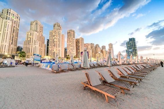 Západ slnka na Marina Beach v Dubaji s plážovými ležadlami a mrakodrapmi.