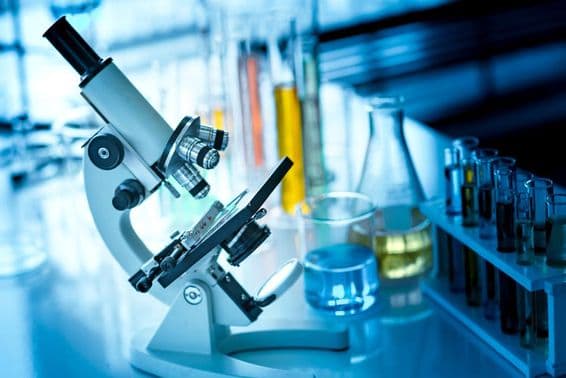 Mikroskop na stole s chemickými skúmavkami a sklárenskými potrebami.