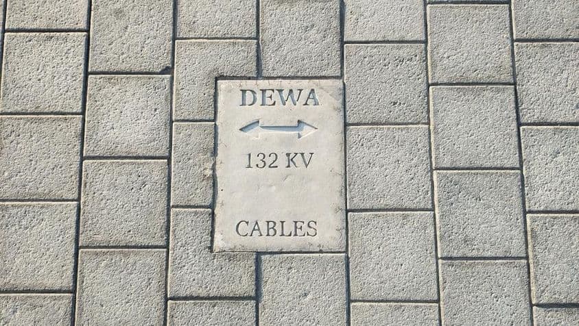 Značka varujúca pred káblami na podlahe z kamenných dlaždíc v Dubaji.
